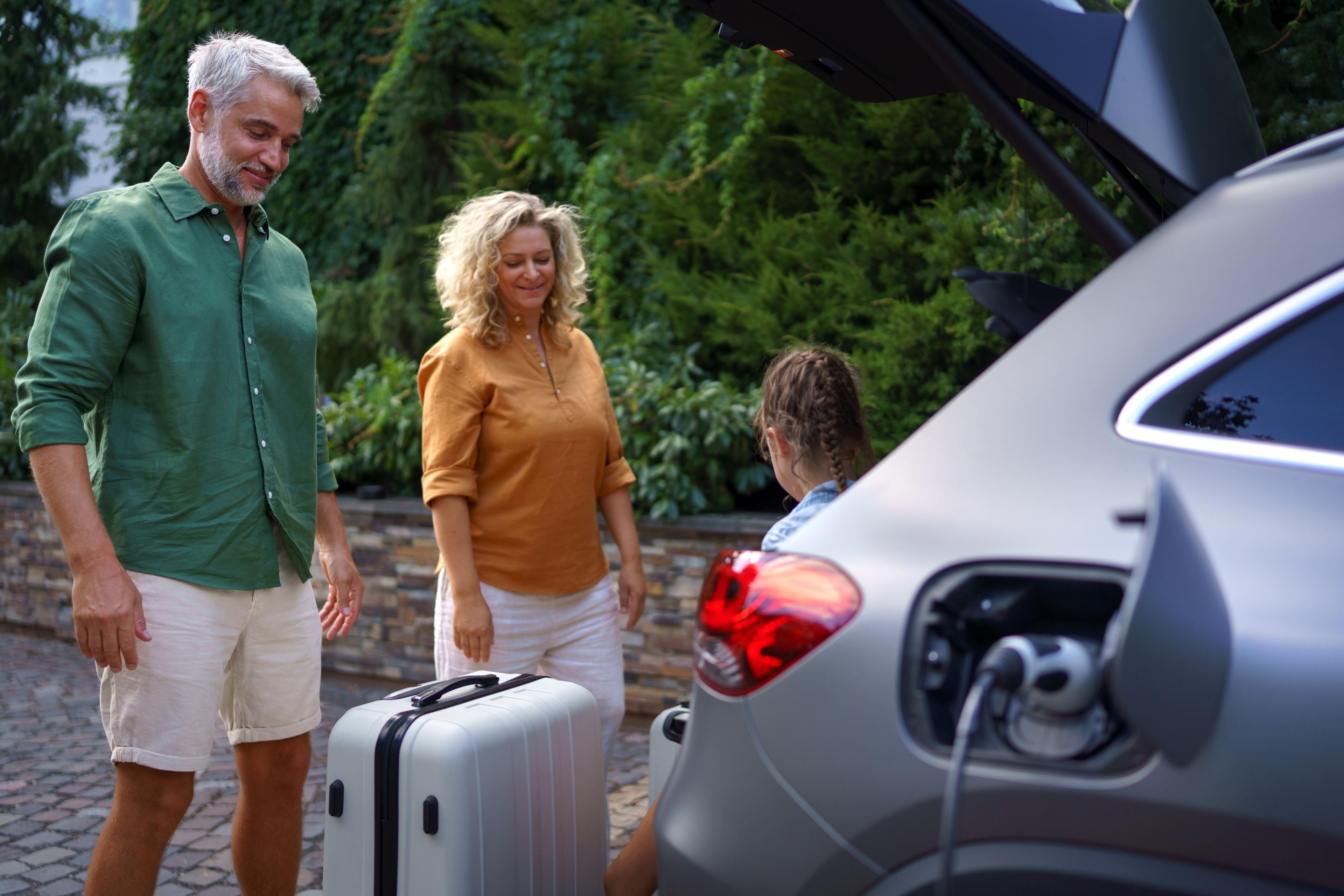 Familie lädt Gepäck aus ladendem E-Auto
